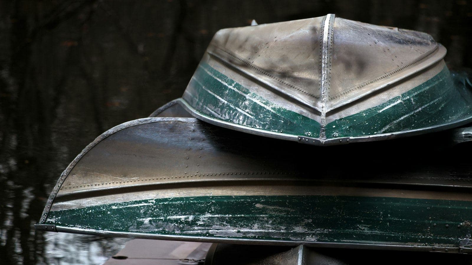 Dois barcos de alumínio empilhados de casco para cima, com a superfície fosca e marcada pelo tempo