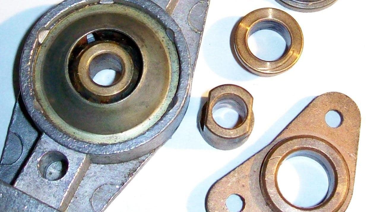 Buchas de bronze sinterizado de vários formatos ao lado de uma tampa de motor com a bucha montada