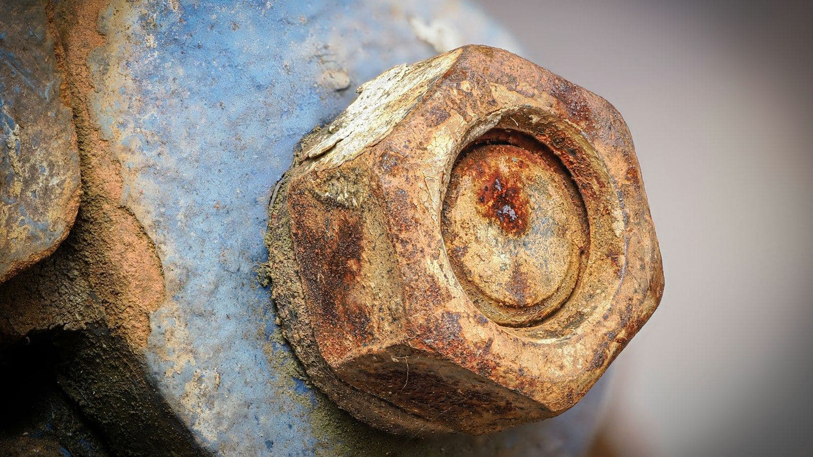 Cabeça de parafuso sextavado tomada pela ferrugem em uma peça de metal pintada de azul
