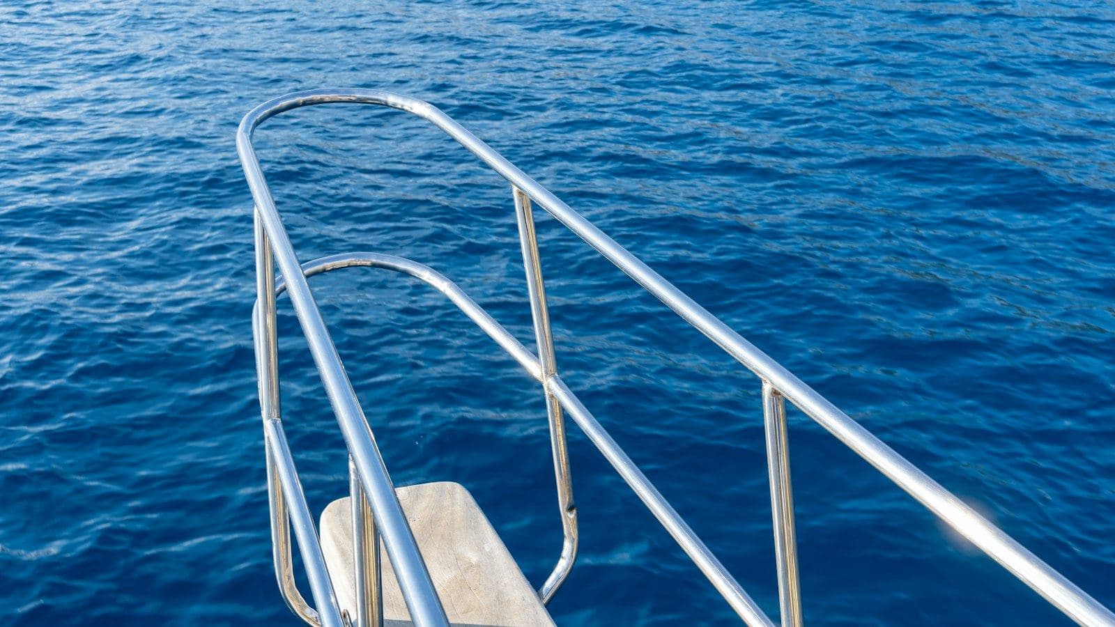 Guarda-corpo de aço inox polido na proa de um barco, sobre o mar azul