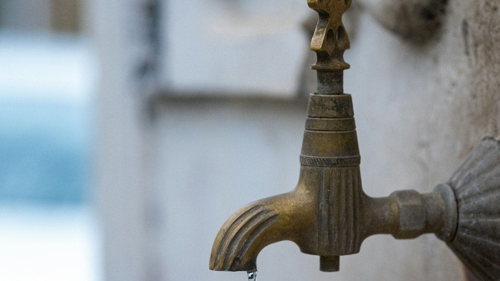Torneira antiga de latão escurecida pelo tempo, presa a uma parede clara