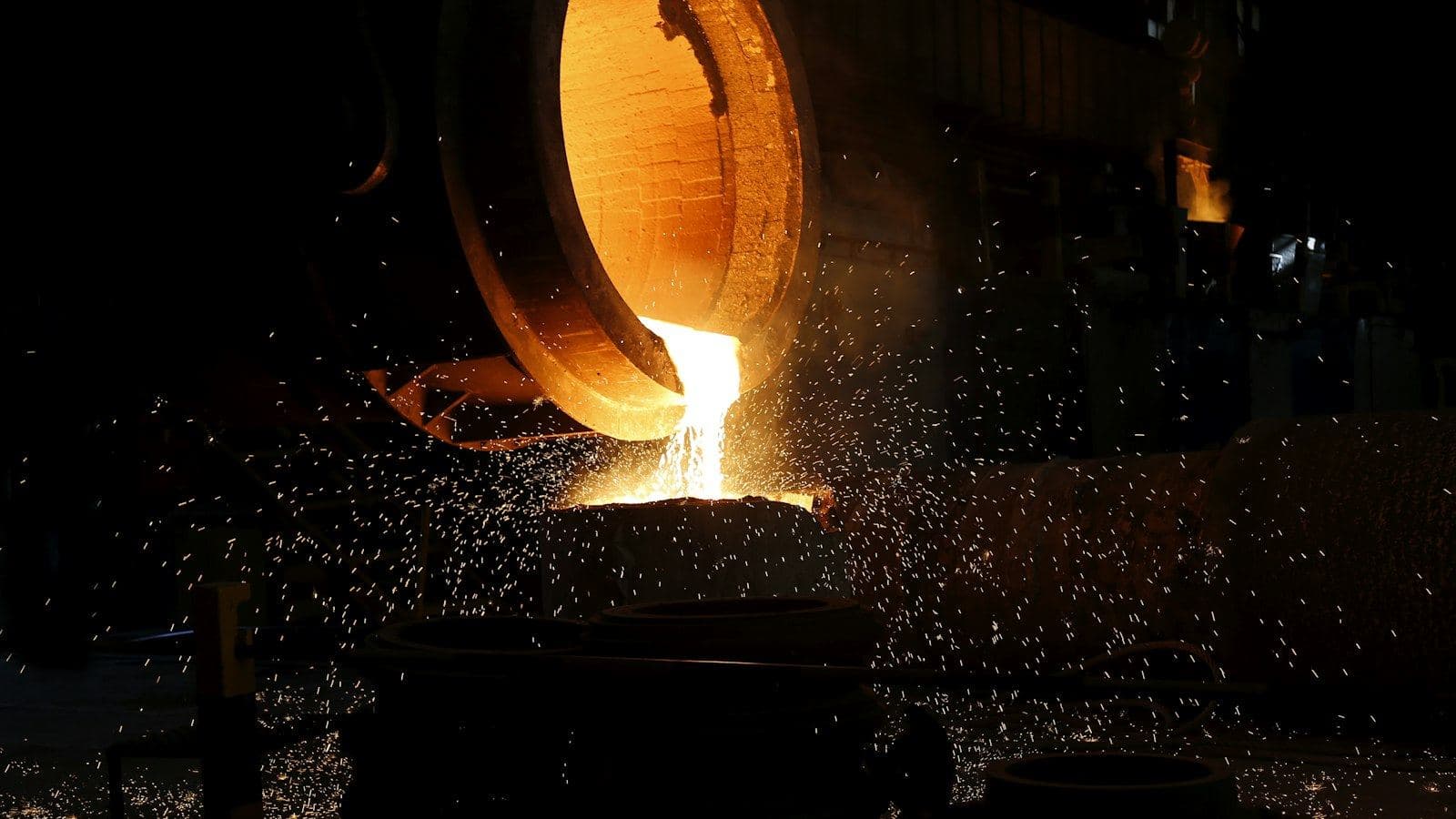 Panela de fundição despejando metal líquido incandescente, com faíscas ao redor